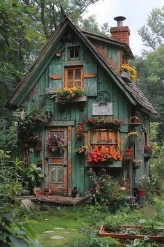 a green house with lots of windows and flowers on the front door, surrounded by greenery