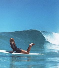 a woman is laying on her surfboard in the ocean while riding a large wave