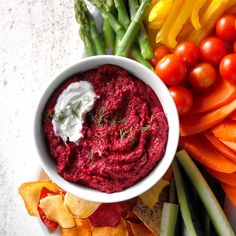 a white bowl filled with red dip surrounded by vegetables