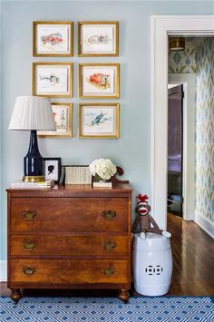 a dresser with pictures on the wall above it and a lamp next to it in a living room