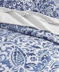 a bed with blue and white sheets on top of it's headboard next to a pillow