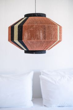 a wooden light hanging from a ceiling in a room with white walls and pillows on the bed