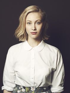 a woman with blonde hair wearing a white shirt and floral skirt, looking at the camera