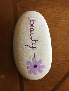 a painted rock with the word happy written on it and a flower in purple ink