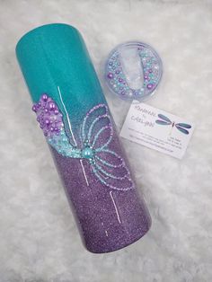 a purple and teal colored tumbler next to a tag on a white surface