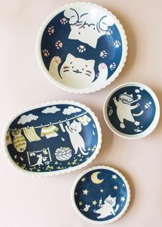 three plates with cats painted on them sitting next to each other in front of a pink wall