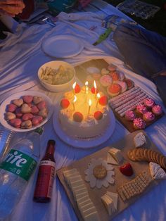 a birthday cake with lit candles surrounded by snacks