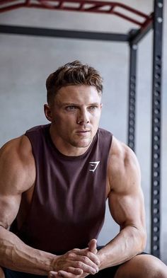 a man sitting on the ground in front of a gym rack with his arms crossed