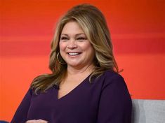 a woman sitting on top of a gray couch next to a red and orange wall