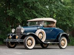 an old model car is parked in front of some trees