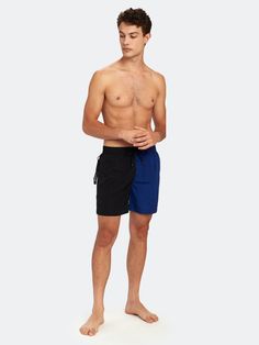 a man standing in front of a white background wearing black and blue swim trunks with no shirt on