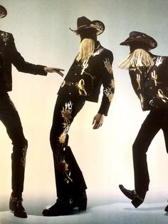 three men dressed in black and gold are dancing with hats on their heads, one wearing a cowboy hat