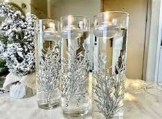 three glass vases sitting on top of a table covered in frosted branches and candles