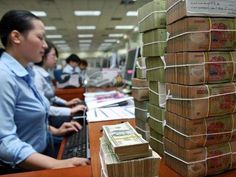 two women sitting at a desk with stacks of money in front of them