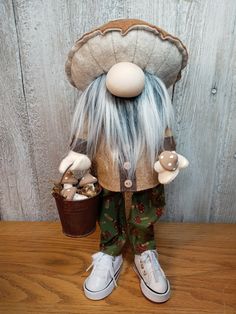 a stuffed animal with long white hair and green pants, holding two small baskets filled with mushrooms