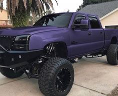 a purple truck parked in front of a house with large tires on it's wheels