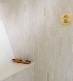 a bathroom with white tile and gold accents on the shower wall, along with a wooden tray