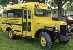 an old yellow school bus parked in the grass near some trees and other vehicles behind it