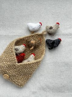 three small knitted chickens sitting in a bag on a tablecloth with buttons and thread