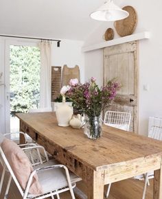 a wooden table topped with vases filled with flowers next to two white metal chairs