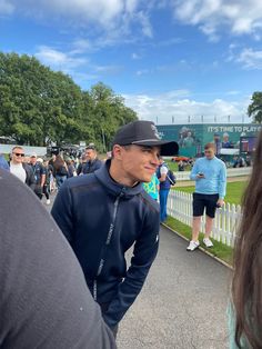 a man in a black hat and jacket standing next to a white fence with other people