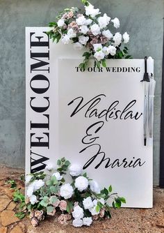 a wedding sign with flowers on it sitting in front of a wall that says welcome to the groom and bride