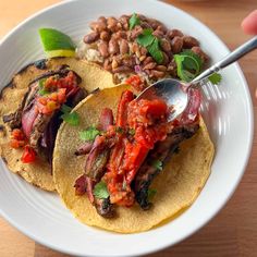 two tacos with meat, beans and garnishes on a white plate