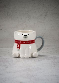 a ceramic bear mug with a red scarf around its neck and eyes, sitting on a gray surface