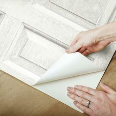 two hands are opening an envelope on the floor next to a wooden paneled door