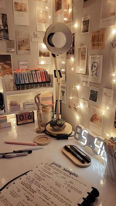 a desk with many items on it and lights strung up behind the desk area, along with an alarm clock