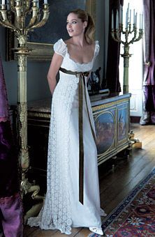 a woman in a white dress standing next to a gold candelabra and chandelier