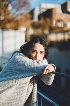 a woman leaning on a railing with her arms over her shoulder and looking at the camera