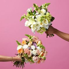 two bouquets of flowers are being held by three hands against a pink background with white and orange flowers