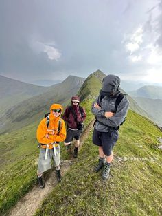 three people hiking up a grassy hill with mountains in the background