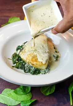 someone is dipping sauce on some food in a white bowl with spinach leaves around it