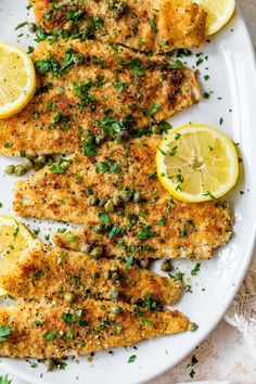 a white plate topped with fish covered in herbs and lemons on top of a table