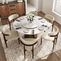 a dining room table with white chairs and plates on the top, surrounded by an area rug