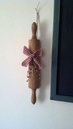 a wooden doll hanging on the wall next to a black frame with a pink gingham bow