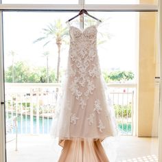 a wedding dress hanging on a rack in front of a window with palm trees outside