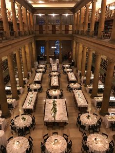 a large library filled with tables and chairs covered in white tablecloths next to tall columns