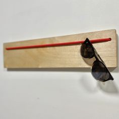 a pair of sunglasses hanging on a wooden wall mounted eyeglass holder with red string