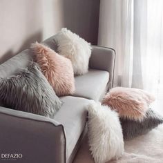 four pillows on the back of a couch in front of a window with white curtains