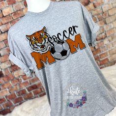 Pick yourself up one of these fun and spirit-filled Tigers spirit shirts. This shirt is sure to impress your friends and make them want one for themselves. Show your soccer mom spirit.  It's a very soft shirt in an athletic heather (gray) color. The shirt is made of 100% polyester but has a cotton feel.  To get the best wear from your shirt make sure to  1. Wash in cold water 2. Tumble dry low 3. Do not iron on design area 4. Do not use fabric softener  unisex sizing. Design color orange Team Spirit Shirts, School Spirit Shirts, Tiger Shirt, Team Mom, Mom Tshirt, Pick Yourself Up, Spirit Shirts