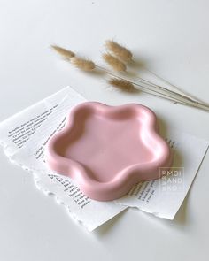 a pink bowl sitting on top of a piece of paper next to some dried grass