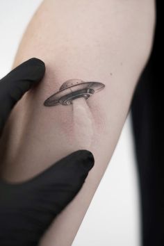 a person with a black glove on their arm holding up a small tattoo in the shape of a flying saucer