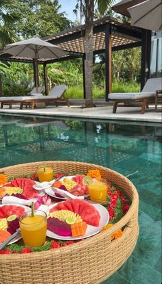 a basket filled with watermelon slices and juices next to a swimming pool