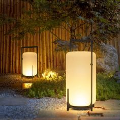 two lights are lit up in front of a bamboo fence at night with rocks and grass