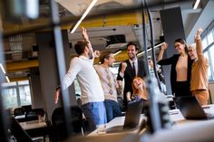 a group of people standing in an office with their arms up and one woman raising her hand