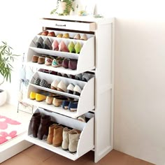 a white shoe rack filled with lots of pairs of shoes next to a potted plant