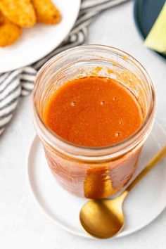 a glass jar filled with sauce sitting on top of a white plate next to a spoon